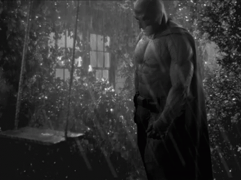 A Black And White Photo Of A Man In A Batman Costume Standing In Front Of A Window . GIF