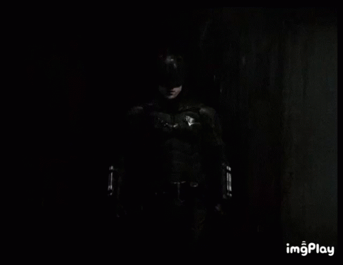A Black And White Photo Of A Man In A Batman Costume Standing In The Dark . GIF