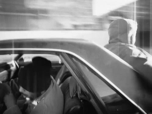 A Black And White Photo Of A Man In A Hoodie Driving A Car GIF