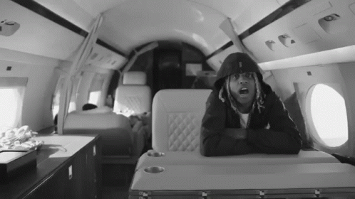 a black and white photo of a man in a hoodie sitting on a plane