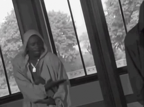 A Black And White Photo Of A Man In A Hoodie Standing In Front Of A Window GIF