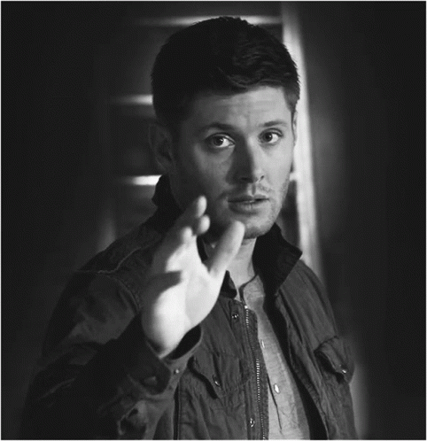 A Black And White Photo Of A Man In A Jacket Making A Gesture With His Hand GIF