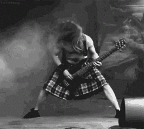 A Black And White Photo Of A Man In A Kilt Playing A Guitar On Stage . GIF