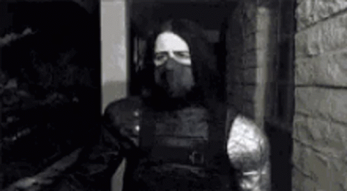 A Black And White Photo Of A Man In A Mask Standing In Front Of A Brick Wall . GIF