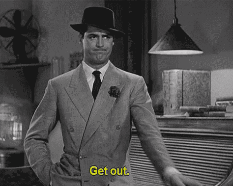 A Black And White Photo Of A Man In A Suit And Hat Pointing At Something . GIF