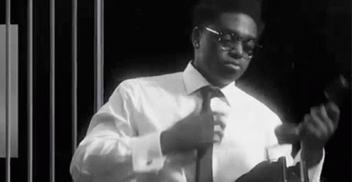A Black And White Photo Of A Man In A Suit And Tie Adjusting His Tie . GIF