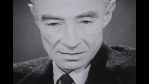A Black And White Photo Of A Man In A Suit And Tie Looking At The Camera . GIF
