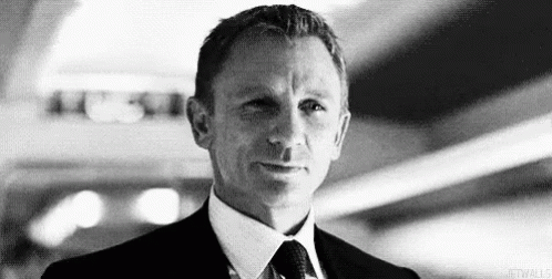 A Black And White Photo Of A Man In A Suit And Tie Looking At The Camera . GIF