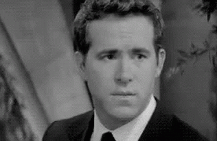 A Black And White Photo Of A Man In A Suit And Tie Making A Face . GIF