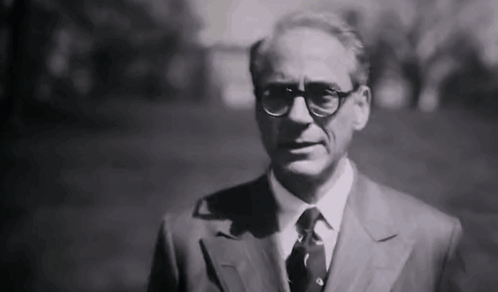 A Black And White Photo Of A Man In A Suit And Tie Standing In A Park . GIF