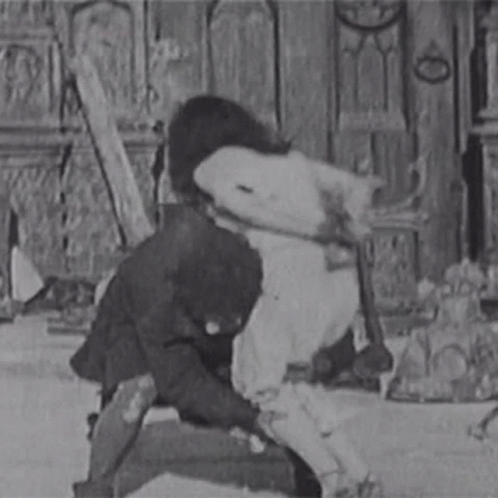 A Black And White Photo Of A Man In A Suit Holding A Woman 'S Leg . GIF