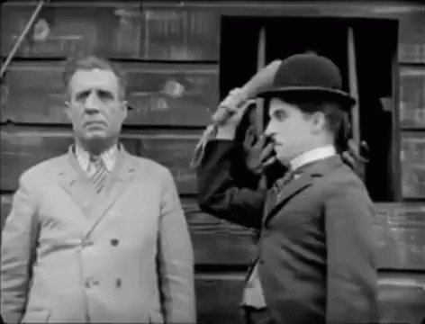A Black And White Photo Of A Man In A Suit Saluting Another Man In A Hat . GIF
