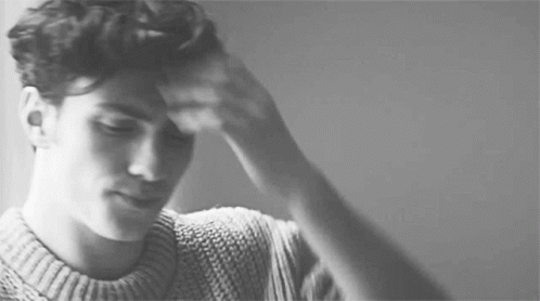 a black and white photo of a man in a sweater holding his head .