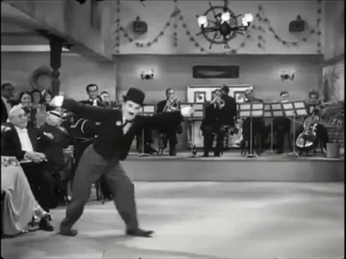 A Black And White Photo Of A Man In A Top Hat Dancing In Front Of An Orchestra GIF