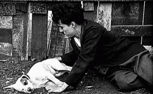 A Black And White Photo Of A Man Kneeling Down With A Dog . GIF