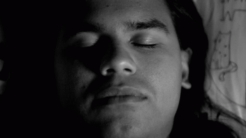 A Black And White Photo Of A Man Laying Down With His Eyes Closed . GIF