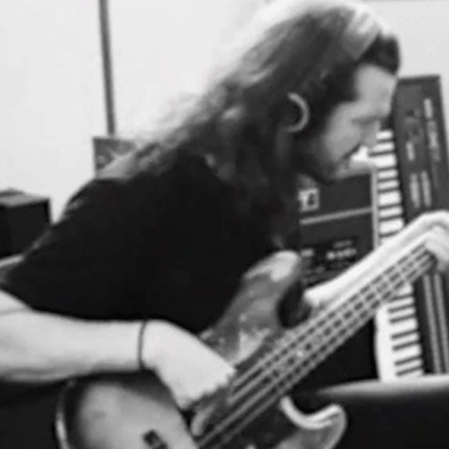 a black and white photo of a man playing a bass guitar in a recording studio .