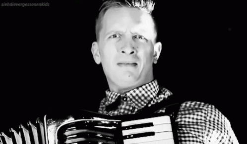 A Black And White Photo Of A Man Playing An Accordion GIF