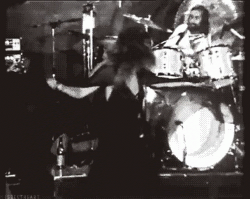 A Black And White Photo Of A Man Playing Drums In Front Of A Drum Set GIF