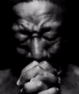 a black and white photo of a man praying with his eyes closed .