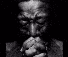 A Black And White Photo Of A Man Praying With His Hands Folded In Front Of His Face . GIF