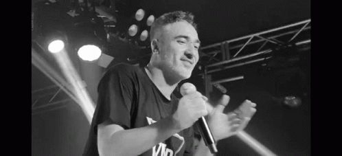 A Black And White Photo Of A Man Singing Into A Microphone On Stage . GIF