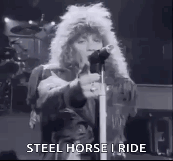 A Black And White Photo Of A Man Singing Into A Microphone On Stage . GIF