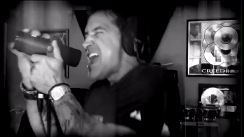 A Black And White Photo Of A Man Singing Into A Microphone With A Creed Poster Behind Him GIF