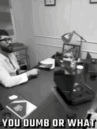 A Black And White Photo Of A Man Sitting At A Desk With The Words You Dumb Or What Above Him GIF