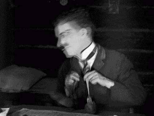 A Black And White Photo Of A Man Sitting At A Table With A Fork And Knife . GIF
