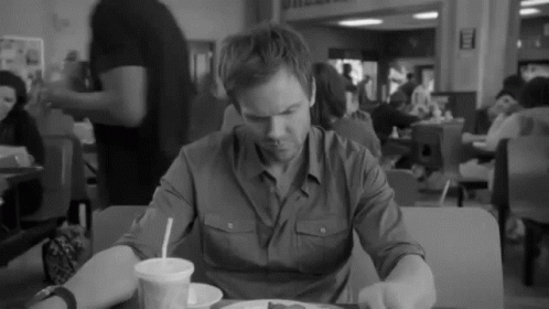 A Black And White Photo Of A Man Sitting At A Table With A Plate Of Food GIF