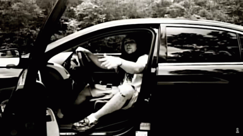 A Black And White Photo Of A Man Sitting In A Car With The Door Open GIF