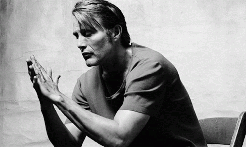 A Black And White Photo Of A Man Sitting In A Chair With His Hands Folded In Prayer . GIF