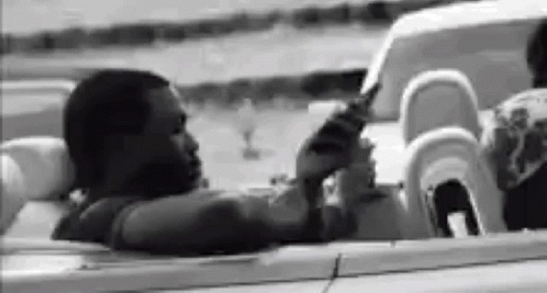 A Black And White Photo Of A Man Sitting In A Convertible . GIF