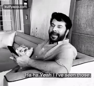 A Black And White Photo Of A Man Sitting On A Couch Holding A Cell Phone And Laughing . GIF