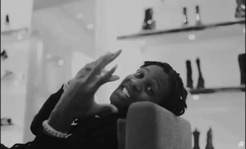 A Black And White Photo Of A Man Sitting On A Couch With His Hands Up . GIF