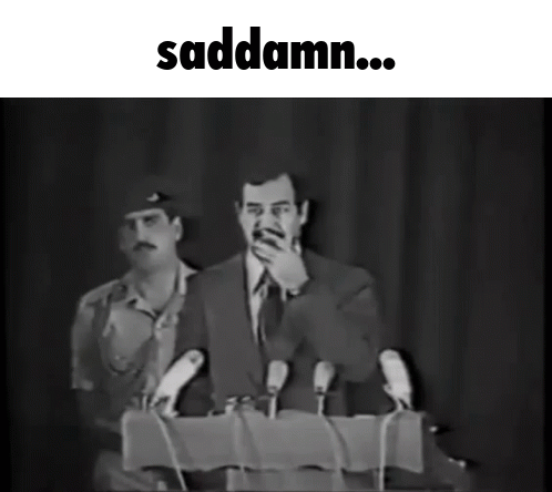 A Black And White Photo Of A Man Speaking Into Microphones With The Words Saddamn Below Him GIF