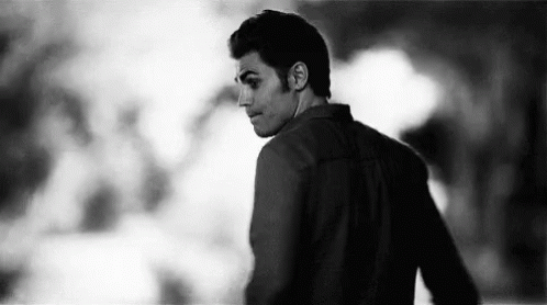 A Black And White Photo Of A Man Standing In A Dark Room Looking Over His Shoulder . GIF