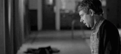 A Black And White Photo Of A Man Standing In A Hallway Looking Down . GIF