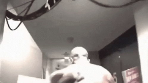 A Black And White Photo Of A Man Standing In A Room With A Ceiling Fan . GIF