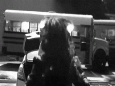 A Black And White Photo Of A Man Standing In Front Of A School Bus GIF