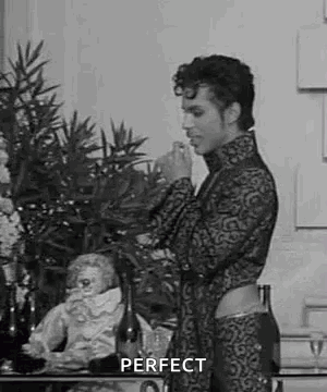 A Black And White Photo Of A Man Standing In Front Of A Table With A Bottle Of Wine And A Statue . GIF