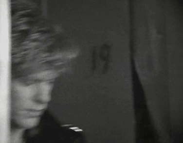 A Black And White Photo Of A Man Standing In Front Of A Wall . GIF