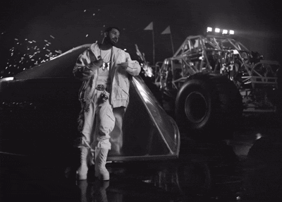 A Black And White Photo Of A Man Standing Next To A Monster Truck At Night GIF