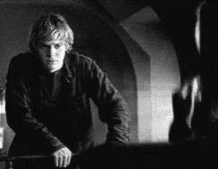 A Black And White Photo Of A Man Standing Next To A Wall Holding A Knife . GIF