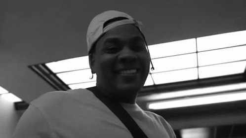 A Black And White Photo Of A Man Wearing A Baseball Cap And Smiling GIF