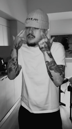 A Black And White Photo Of A Man Wearing A Beanie That Says M & M GIF