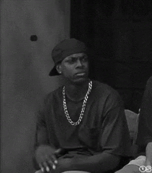 A Black And White Photo Of A Man Wearing A Hat And A Chain Around His Neck . GIF