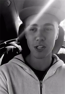 A Black And White Photo Of A Man Wearing A Hat And A Hoodie In A Car . GIF