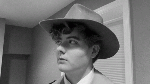 A Black And White Photo Of A Man Wearing A Hat And A Suit GIF
